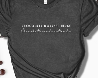 May include: Dark gray t-shirt with the text "CHOCOLATE DOESN'T JUDGE Chocolate understands" in white. The shirt is surrounded by chocolate cookies and chocolate pieces.