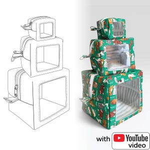 May include: A stacked cat bed set with three cube-shaped beds. The beds are covered in a green fabric with a cat pattern and have clear viewing windows. Each bed has a zippered top and a striped interior.