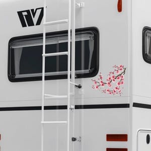 May include: White RV exterior with a black window, ladder, and cherry blossom decal. The decal features pink flowers and brown branches. The RV has black stripes and a red light.