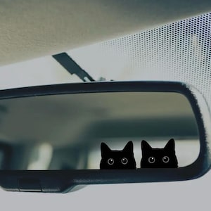 May include: A rearview mirror with two black cat silhouettes peeking out from behind the mirror.