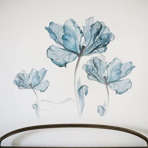 May include: A wall decal featuring three blue watercolor flowers with delicate petals and stems. The flowers are arranged in a cluster, with the largest flower at the top and the smallest flower at the bottom. The decal is perfect for adding a touch of elegance and nature to any room.