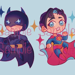Może przedstawiać: Ilustracja Batmana i Supermana w stylu chibi. Batman ma na sobie ciemnoniebieski kostium z peleryną, a Superman niebiesko-czerwony kostium z peleryną. Obie postacie mają duże oczy i są na jasnoniebieskim tle.