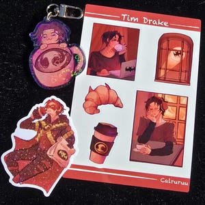 May include: A selection of fan art stickers and a keychain featuring a character in red and black. The stickers depict the character with a coffee cup, a croissant, and a laptop with a bat symbol. The keychain shows a character inside a teacup.