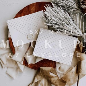 May include: A white card with a grey polka dot pattern and a wax seal on a wooden tray with a brown ribbon and a snowy pine branch. The card is a 5x7 size and the text on the card reads "5x7 Ratio A7 Envelope".