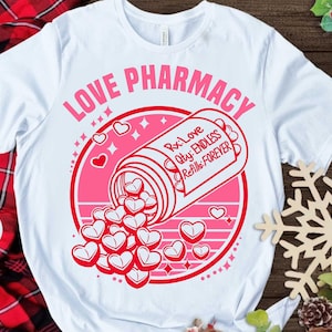 May include: White t-shirt with a pink and red graphic design. The graphic features a pill bottle with hearts spilling out and the text "Love Pharmacy Rx:Love Qty: Endless Refills:Forever".