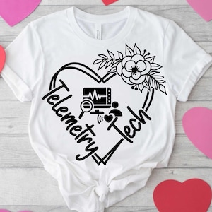 May include: White t-shirt with a black heart-shaped design. The design includes the words "Telemetry Tech", a floral arrangement, and medical monitoring symbols. The shirt is displayed on a light wood-grain surface with pink and red heart cutouts.