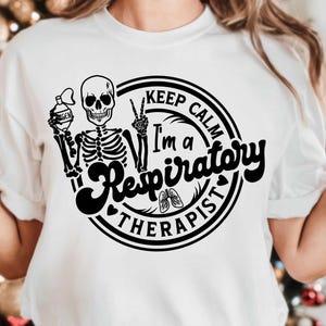 May include: White t-shirt with a black graphic featuring a skeleton holding an oxygen tank and making a peace sign. The text reads "Keep Calm I'm a Respiratory Therapist" in a circular design with a heart and lungs.