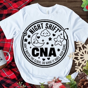 May include: White t-shirt with a black and white graphic design. The graphic features a circle with the text "Night Shift CNA Don't Watch The Clock; Do What It Does. Keep Going." inside. The circle also includes a crescent moon, a cloud, a star, and a stethoscope.