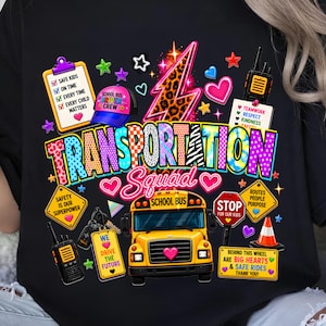May include: A black t-shirt featuring a colorful graphic with a yellow school bus, a leopard print lightning bolt, and text reading Transportation Squad. The design includes icons like a clipboard, walkie-talkies, a stop sign, and a traffic cone.