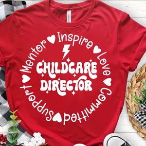 May include: A red t-shirt featuring the words "Childcare Director" in a white, retro font, encircled by words such as "Inspire," "Love," and "Support." The design incorporates hearts and a lightning bolt.