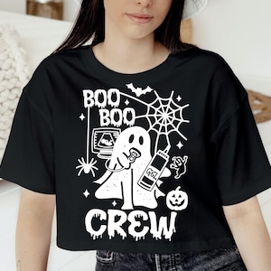 May include: Black crop top with a white graphic featuring a ghost with a pacifier, ultrasound image, spiderweb, and the text "BOO CREW". A bat, spider, and pumpkin are also included in the design.