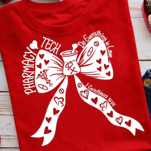 May include: A red t-shirt with a white graphic featuring a mortar and pestle, hearts, and the words "Pharmacy Tech." The design includes the phrase "Do Everything in Love" and the Bible verse 1 Corinthians 16:14.