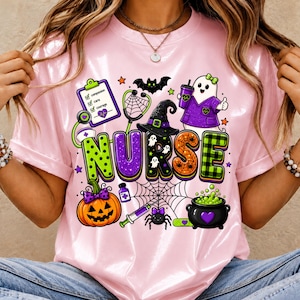May include: A light pink t-shirt featuring a graphic with the word NURSE in colorful, patterned letters. The design includes a clipboard, stethoscope, witch hat, ghost, pumpkin, spider, syringe, and a cauldron, all with Halloween-themed accents.