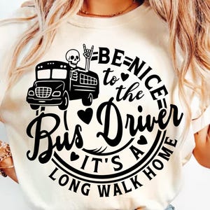 May include: Cream-colored t-shirt with a black graphic featuring a school bus, a skeleton, and the text "BE NICE to the Bus Driver IT'S A LONG WALK HOME". The design includes hearts and a rock-on hand gesture.