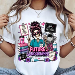 May include: A white t-shirt featuring a graphic of a skeleton wearing a teal scrub top, pink sunglasses, and a leopard print headband. The design includes an ultrasound machine, books, a clipboard with text, and the words Future Sonographer.