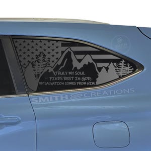 May include: A light blue car window decal featuring an American flag design with mountains and trees. The decal includes the text "TRULY MY SOUL FINDS REST IN GOD; MY SALVATION COMES FROM HIM!" and the brand name "SMITH CREATIONS".