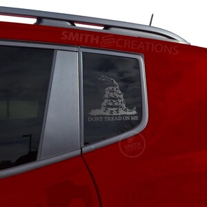 May include: A red vehicle window with a silver "Don't Tread on Me" decal featuring a coiled rattlesnake. The decal is on the rear passenger window. The text "DON'T TREAD ON ME" is below the snake.