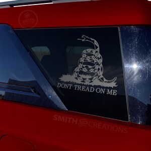 May include: A red car with a black window sticker featuring a coiled snake with the text "Don't Tread On Me".