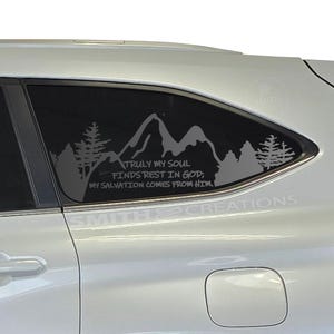 May include: A car window decal featuring a mountain and forest silhouette design. The decal includes the text "TRULY MY SOUL FINDS REST IN GOD; MY SALVATION COMES FROM HIM!" in a stylized font. The decal is applied to a white car.