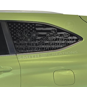 May include: A green vehicle with a window decal featuring an American flag design with floral silhouettes. The decal includes the text "SMITH CREATIONS". The flowers are in various shapes and sizes.