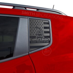May include: A red vehicle with a window decal featuring the American flag, a coiled snake, and the text "DON'T TREAD ON ME." The decal is silver and the vehicle has a black roof rack.