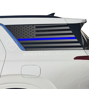 May include: A white SUV with a rear window graphic featuring the American flag with a blue line. The graphic is a stylized representation of the flag, with stars and stripes. The text "SMITH CREATIONS" is visible.