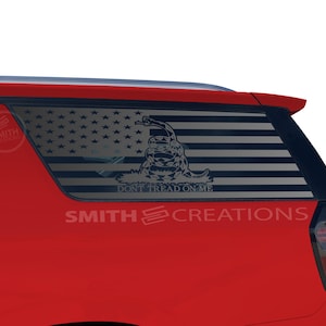 May include: A red vehicle with a window decal featuring the American flag and the phrase "DON'T TREAD ON ME." The decal also includes a coiled snake. The text "SMITH CREATIONS" is below the window.