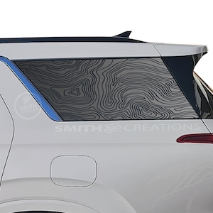 May include: A white SUV with a black and white topographic map design on the rear window. The design is a vinyl decal and features the text "SMITH CREATIONS".