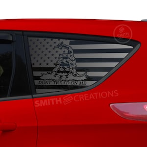 May include: A red car with a window decal featuring the American flag and a coiled snake with the words "DON'T TREAD ON ME". The decal is black and white.