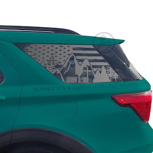 May include: A teal SUV with a window decal featuring an American flag design, mountains, trees, and a cross. The text "JOHN 3:16" is visible. The decal is on the rear window.