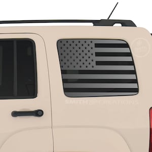 May include: A tan SUV with a black American flag decal on the rear window. The flag design features gray stars and stripes. The text "SMITH CREATIONS" is visible on the vehicle.