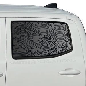 May include: White truck with a rear window featuring a black topographic map design. The window graphic has a swirling, layered pattern. The text "SMITH CREATIONS" is visible on the vehicle.