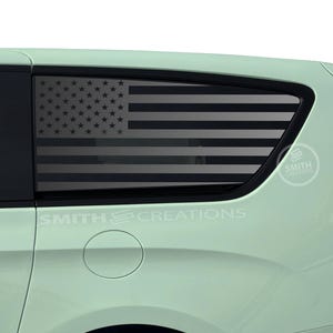 May include: A light green minivan with a black American flag decal on the rear window. The decal is a silhouette of the American flag with black stars and stripes.
