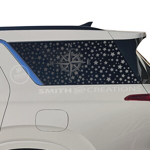 May include: White SUV with a rear window graphic featuring a star-filled design and a compass rose. The graphic is overlaid on the window, creating a patriotic theme. The text "SMITH CREATIONS" is visible on the vehicle.