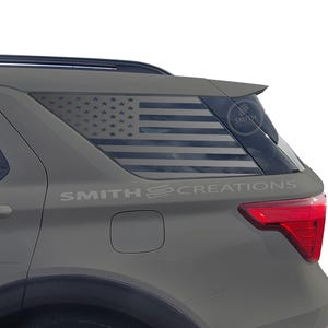 May include: A gray SUV with a rear window decal of the American flag. The decal is in black and white and features the text "SMITH CREATIONS".