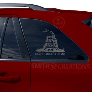 May include: A red car with a black window sticker featuring a coiled snake with the text "Don't Tread On Me".