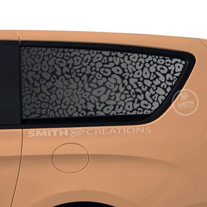 May include: A tan minivan with a black leopard print design on the rear window. The design is a repeating pattern of black spots on a white background. The text "SMITH CREATIONS" is printed on the side of the van.