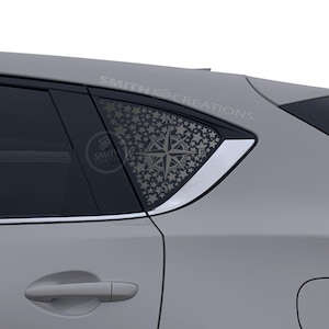 May include: A gray car window decal featuring a compass rose design with a star pattern. The decal is applied to the rear passenger window of a gray car. The text "SMITH CREATIONS" is visible on the car.