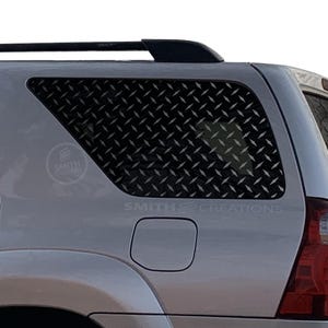 May include: Silver SUV with a diamond plate window guard. The guard is black and covers the rear side window. The text "SMITH CREATIONS" is visible on the vehicle.
