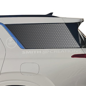 May include: White SUV with a black honeycomb pattern window covering. The text "SMITH CREATIONS" is visible on the vehicle. The rear tail light is red.