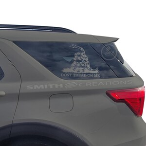 May include: A gray SUV with a "Don't Tread On Me" sticker on the back window. The sticker features a coiled rattlesnake with the words "Don't Tread On Me" below it.