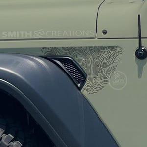May include: Close-up of a section of a light green vehicle. A black vent and tire are visible. A black and white topographic map design is on the side of the vehicle. The text "SMITH CREATIONS" is printed on the vehicle.