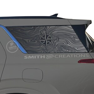 May include: A gray SUV with a compass and topographic map design on the rear window. The design is black and white and includes the text "SMITH CREATIONS". The vehicle's taillight is red.