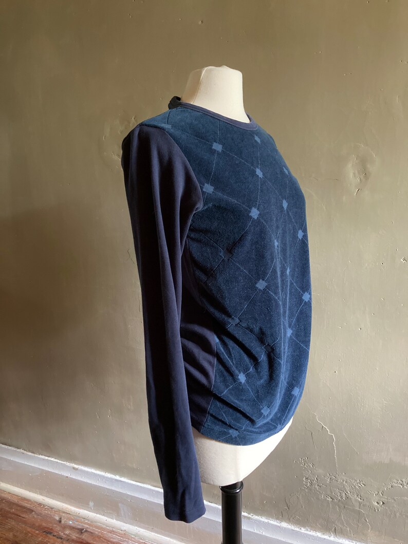 May include: A navy blue long-sleeved shirt with a geometric pattern on the front. The shirt is made of a soft, textured fabric.