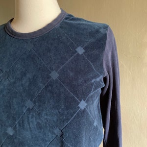 May include: A navy blue long-sleeved shirt with a quilted diamond pattern on the front. The shirt is made of a soft, textured fabric.