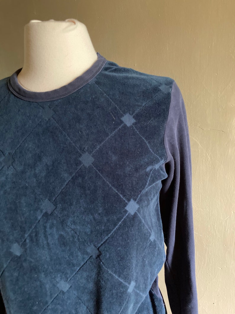 May include: A navy blue long-sleeved shirt with a quilted diamond pattern on the front. The shirt is made of a soft, textured fabric.