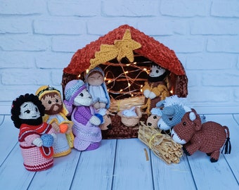 May include: A nativity scene with crocheted figures of Mary, Joseph, baby Jesus, a shepherd, and two animals. The figures are arranged in front of a crocheted stable with a star on top. The scene is decorated with lights.