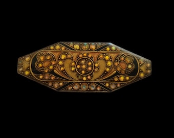 Könnte beinhalten: Eine goldfarbene Brosche mit schwarzem Emaille-Hintergrund und einem Design aus stilisierten Wirbeln und Kreisen. Die Brosche ist mit schillernden Strasssteinen verziert.