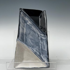 Peut inclure: Un plat de service en céramique avec un design géométrique. Le plat est divisé en deux sections, une noire et une blanche. Le plat est sur un support en acrylique transparent.