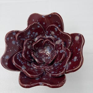 Puede incluir: Escultura de flor de cerámica burdeos, con acabado brillante y detalles moteados. Los pétalos superpuestos crean un efecto tridimensional. Esta pieza decorativa es probablemente para la decoración del hogar.